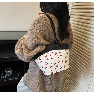 Close-up of white bucket bag with cherry print and black leather strap details