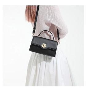 Détail d'un sac à bandoulière noir mat avec fermoir rotatif doré sur un fond blanc