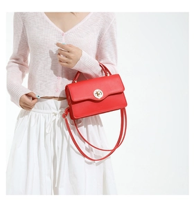 Modèle portant un sac bandoulière rouge avec fermoir doré et finition en cuir lisse
