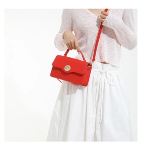 Détail du sac à bandoulière en cuir rouge avec fermoir doré sur un cardigan rose doux