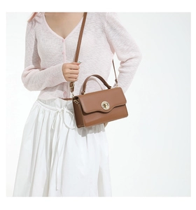 Détail d'un sac bandoulière en cuir marron avec fermoir rotatif en métal et poignée
