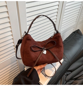 Detail of burgundy suede shoulder bag with a large bow and heart-shaped metal pendant
