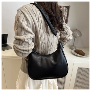 Detail of minimalist black PU leather hobo bag worn by a model in a modern office setting
