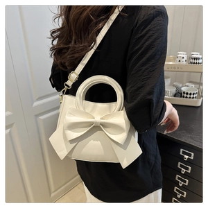 Detail of creamy white leather crossbody bag featuring a large bow and top handle
