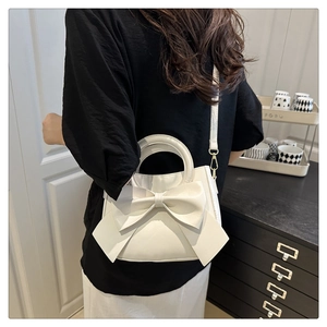 Detail of white PU leather crossbody bag with bow decoration and gold metal hardware