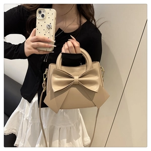 Mirror selfie showing a beige crossbody bag with a large decorative bow and top handle