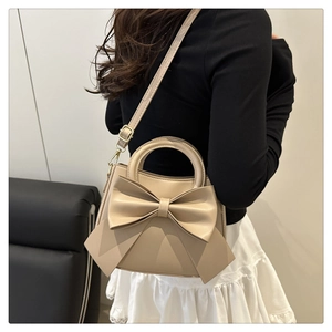 Detail view of beige bow handbag with matte leather and golden metal hardware details