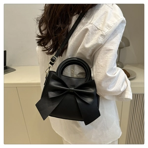 Detail of a black crossbody bag with a large decorative bow and elegant handle