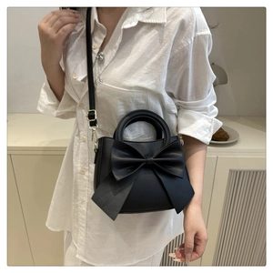 Detail shot of black bucket bag with large decorative bow and adjustable crossbody strap