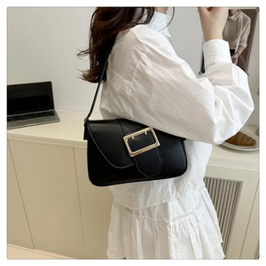 Détail du sac sous l'aisselle en similicuir noir avec fermoir doré sur robe blanche