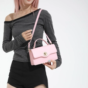 Sac bandoulière en cuir rose avec fermoir rotatif doré porté par un mannequin sur fond blanc
