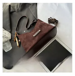 Detail of suede crossbody bag with metal logo, beaded charm, and lifestyle accessories