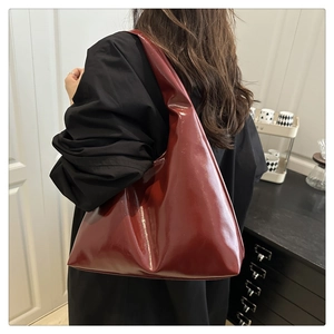Sac fourre-tout triangulaire en cuir verni bordeaux porté à l'épaule par un mannequin