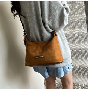 Brown faux suede dumpling bag featuring wooden bead charm and adjustable strap detail