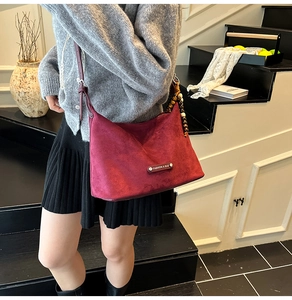 Detail view of burgundy frosted suede crescent bag with beaded strap and metal fashion plaque