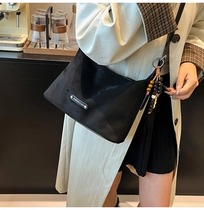 Detail of black suede dumpling bag with a beaded tassel and metal logo on beige coat