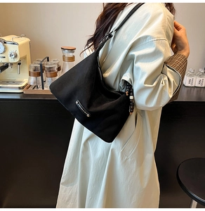 Detail of a black hobo shoulder bag with silver plaque and bead zipper on beige coat