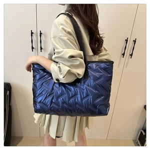 Sac fourre-tout matelassé bleu métallisé porté à l'épaule dans un décor de mode