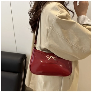 Detalle de bolso de hombro en charol rojo con hebilla de lazo dorado sobre abrigo beige