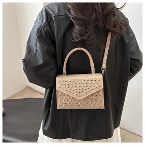 Rear view of a beige crossbody bag with silver studs and tassel on a model wearing leather