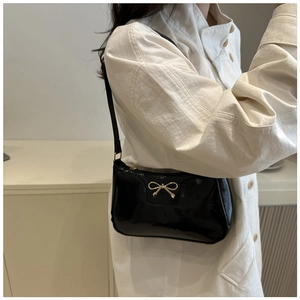 Détail du sac sous le bras en cuir verni noir avec un délicat nœud doré décoratif