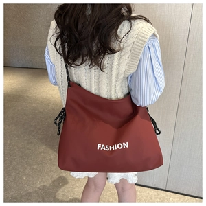Detail of rust red crossbody bag with white FASHION lettering and rope shoulder strap