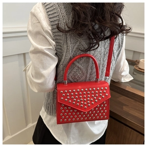 Bright red rivet small square bag being worn as a shoulder bag in a cozy home setting