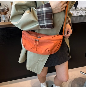 Detail of an orange nylon crescent crossbody bag with zipper accents on model