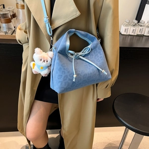 Borsa a mano blu leopardata con ciondolo di peluche indossata su un cappotto cammello