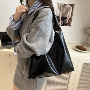 Sac fourre-tout minimaliste en cuir noir brillant présenté dans un cadre chic de bureau
