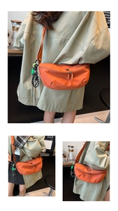 Detail van een feloranje halve maan crossbodytas met een geweven tashanger accessoire