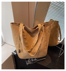 Detail of khaki canvas tote bag with fashion label and front pocket on black shelf
