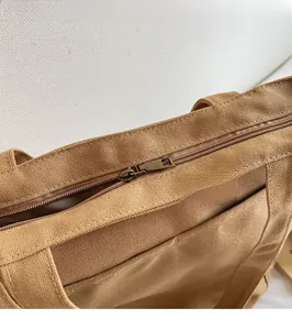 Detail view of smooth metal zipper and thick canvas handle on brown nylon tote bag
