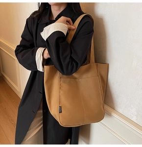 Detail of tan canvas tote bag showing side fashion label and reinforced shoulder strap