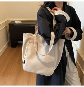 Detail of minimalist beige canvas tote bag with front pocket and fashion label on black suit