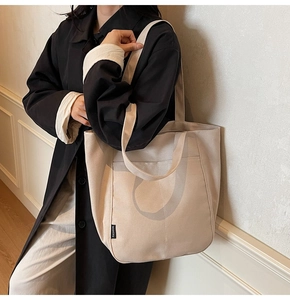 Detail of a large beige canvas tote bag with front pocket and wide shoulder strap