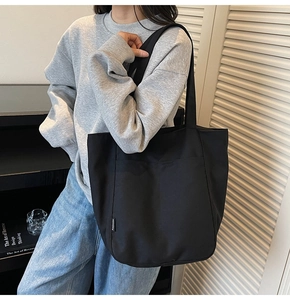 Detail of the black canvas tote bag showing the textured fabric and fashion side label