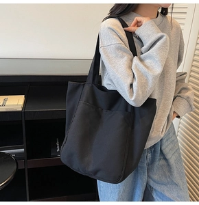 Detail of minimalist black canvas tote bag with large dual pockets and brand side label