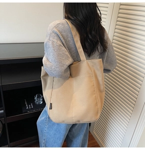 Detailed side view of beige canvas tote bag with fashion label and vertical stitching