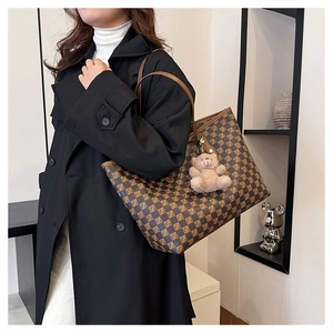 Detail of checkered tote bag with plush bear charm worn with a stylish trench coat