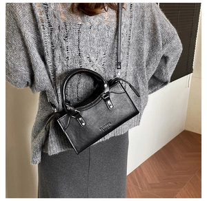 Close-up of minimalist black leather trapezoid handbag with rivet detail and top handle