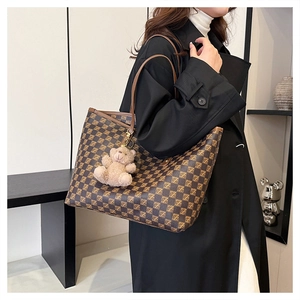 Detail of large tote bag with brown checkered pattern and plush bear charm on model