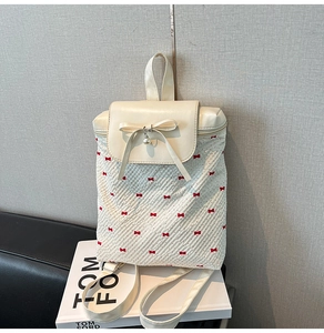Detail of cream backpack with red bow prints and a pearl pendant on the front flap