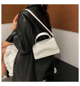Detail of white leather handbag showing parallel stitching and gold hardware on flap