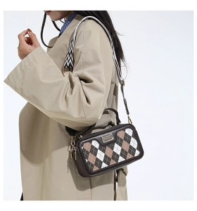 Detail view of plaid crossbody bag featuring wide herringbone strap on a trench coat