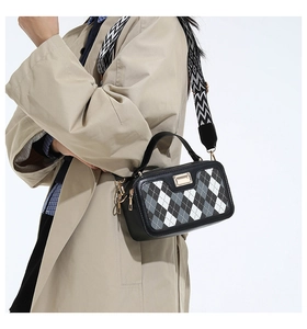 Detail of checkered crossbody bag with wide geometric strap worn on a trench coat