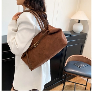 Detail of a brown suede tote bag featuring slim shoulder straps and gold metal buckle