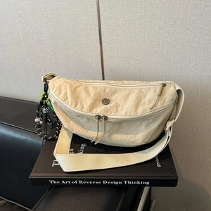 Detail van de crèmewitte nylon crossbodytas in halve maanvorm op een leren bank