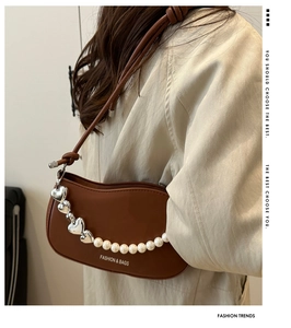 Detail of caramel underarm bag with silver heart and pearl chain on a beige coat