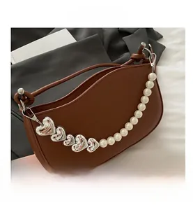 Detail of brown leather saddle bag with heart-shaped metal and pearl decorative chain